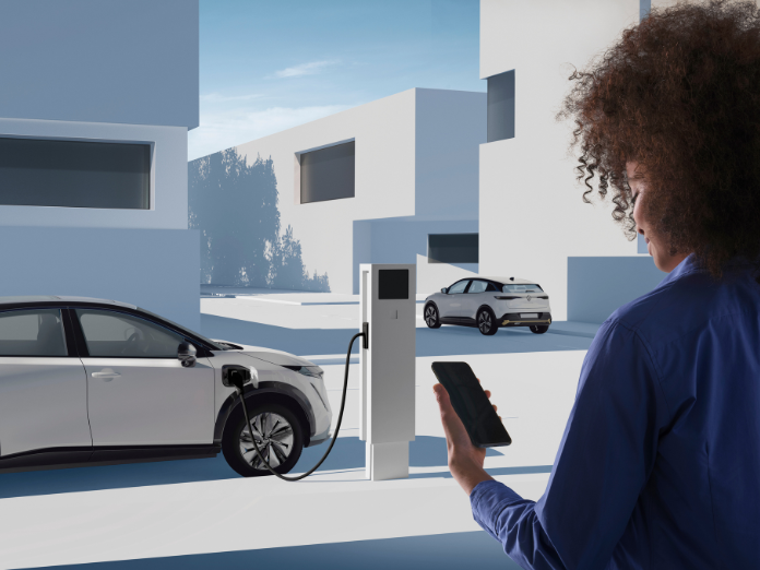 Photo of lady wearing a blue coat holdong a phone while watching a white Renault Megane at an EV charger