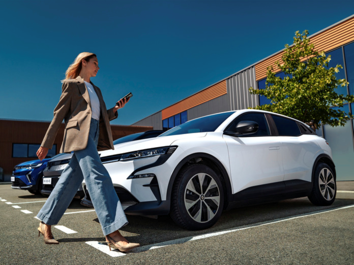 Lady wearing taupe jacket and jeans in front of a white Renault Scenic