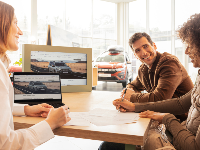 Customers talking to an employee with a picture of a car on a laptop screen and a Dacia in the background
